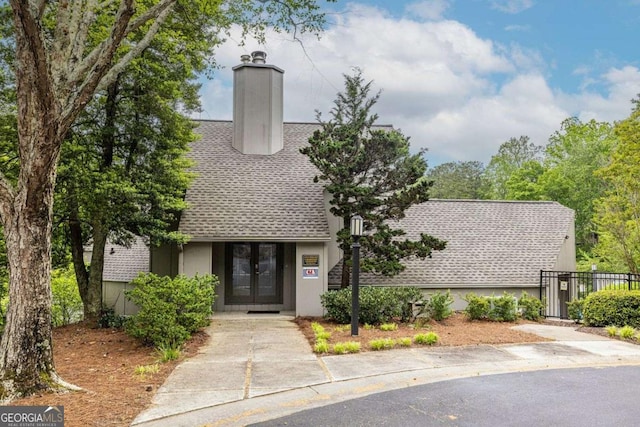 view of front facade featuring french doors, a shingled roof, fence, and a chimney