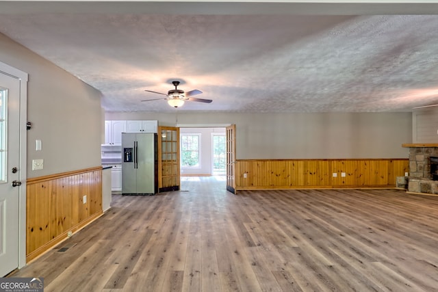 unfurnished living room featuring a wainscoted wall, a ceiling fan, light wood-style flooring, wood walls, and a fireplace