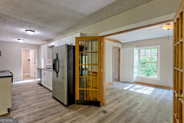 kitchen with stainless steel appliances, white cabinetry, light wood-type flooring, and a textured ceiling