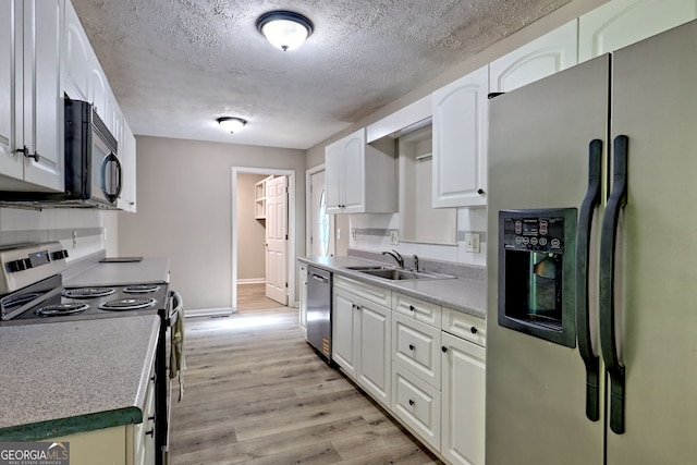 kitchen with appliances with stainless steel finishes, a sink, light wood-style floors, baseboards, and a textured ceiling