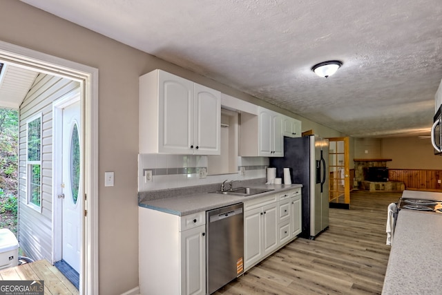 kitchen with appliances with stainless steel finishes, light wood-style floors, white cabinetry, a sink, and a textured ceiling