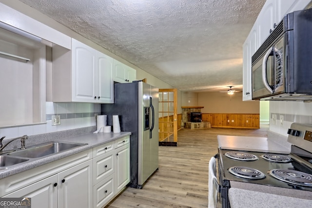kitchen featuring appliances with stainless steel finishes, a sink, light wood-style flooring, white cabinets, and ceiling fan