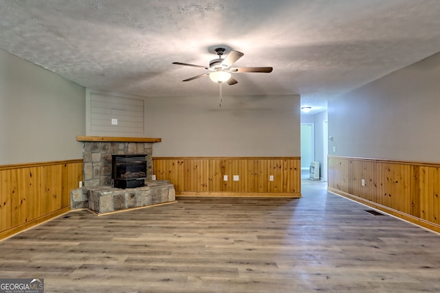 unfurnished living room featuring a wainscoted wall, ceiling fan, wood finished floors, wood walls, and a fireplace
