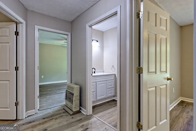 corridor with heating unit, light wood-style flooring, baseboards, a textured ceiling, and a sink