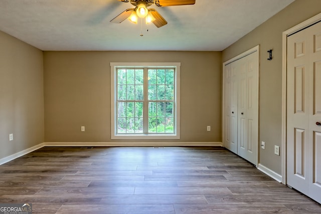 unfurnished bedroom featuring multiple closets, baseboards, wood finished floors, and a ceiling fan