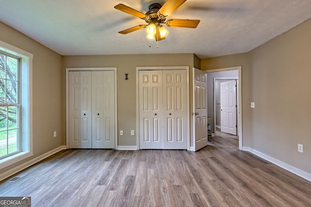 unfurnished bedroom featuring wood finished floors, baseboards, multiple closets, and ceiling fan