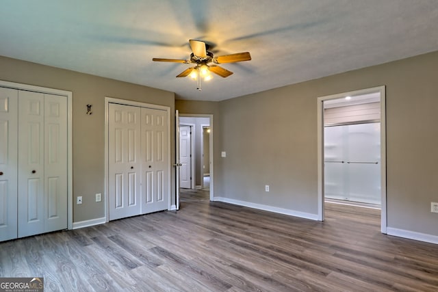 unfurnished bedroom featuring wood finished floors, baseboards, two closets, and connected bathroom