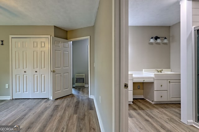 hall with wood finished floors, baseboards, a sink, and heating unit