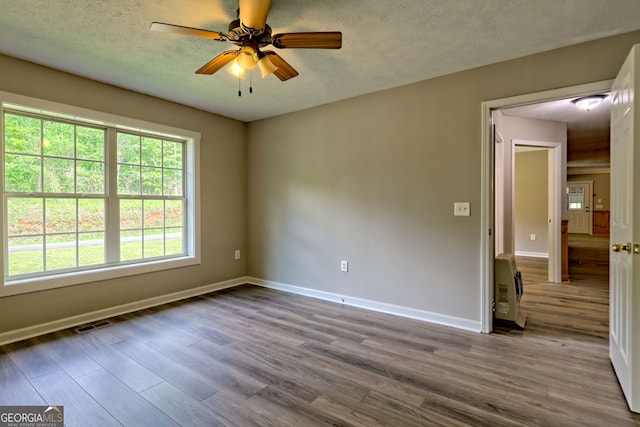 unfurnished room with wood finished floors, heating unit, a ceiling fan, baseboards, and a textured ceiling