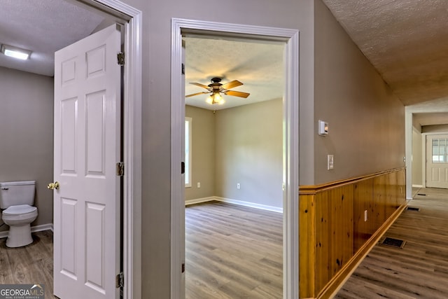 corridor with wood finished floors, a wainscoted wall, a textured ceiling, and wooden walls
