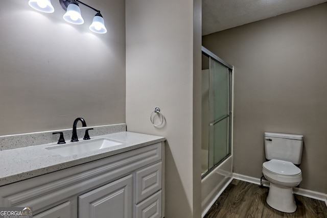 full bath with toilet, wood finished floors, vanity, combined bath / shower with glass door, and baseboards