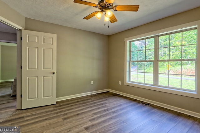spare room with baseboards, dark wood-style floors, and a ceiling fan