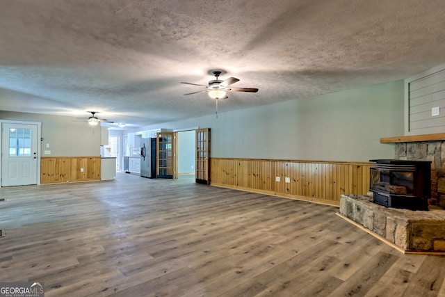 unfurnished living room with ceiling fan, wood finished floors, wainscoting, a textured ceiling, and wooden walls