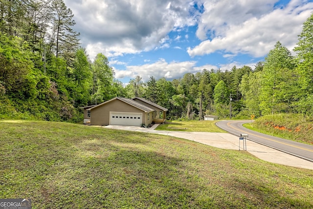 view of front of house featuring a front lawn, driveway, a garage, and a forest view