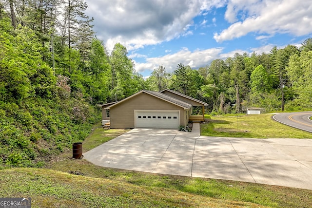 view of front facade featuring concrete driveway, a front lawn, a view of trees, and a garage