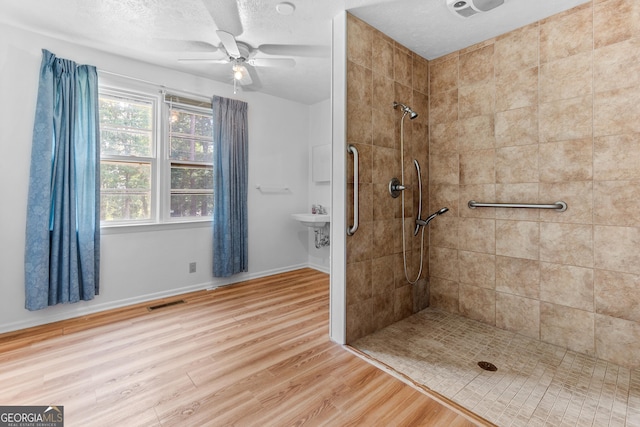 144 Bryant Rd, Cordele, GA 31015 - bathroom with a tile shower, wood finished floors, a ceiling fan, baseboards, and a textured ceiling