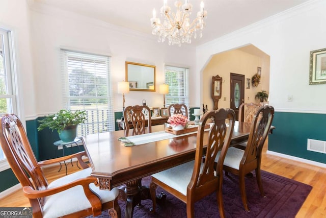 dining area with a chandelier, ornamental molding, plenty of natural light, wood finished floors, and baseboards