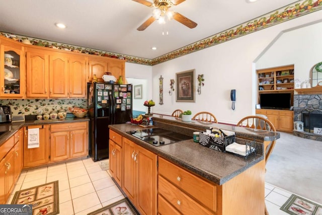 kitchen with black fridge with ice dispenser, dark countertops, stovetop with downdraft, a ceiling fan, and light tile patterned flooring