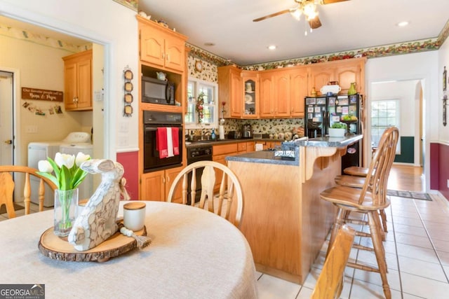kitchen featuring black appliances, washer and dryer, ceiling fan, a center island, and glass insert cabinets