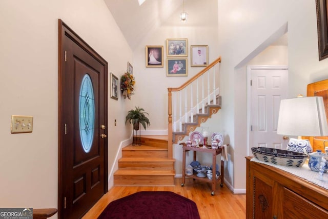 entrance foyer featuring stairs, light wood-type flooring, lofted ceiling, and baseboards