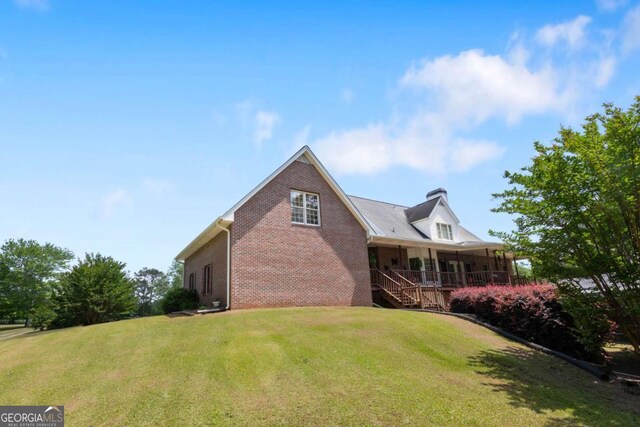 view of home's exterior with brick siding, a yard, a porch, a chimney, and stairway