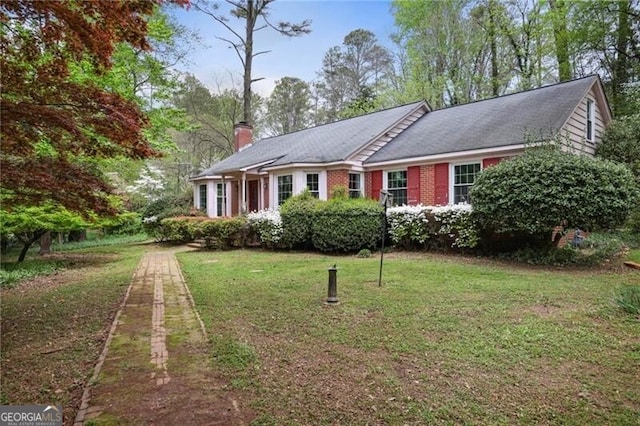 ranch-style home featuring a front yard, a chimney, and brick siding