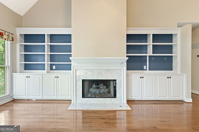 unfurnished living room with plenty of natural light, wood finished floors, vaulted ceiling, and a fireplace