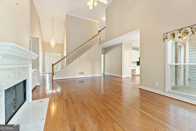 unfurnished living room featuring high vaulted ceiling, a high end fireplace, stairway, baseboards, and light wood-type flooring