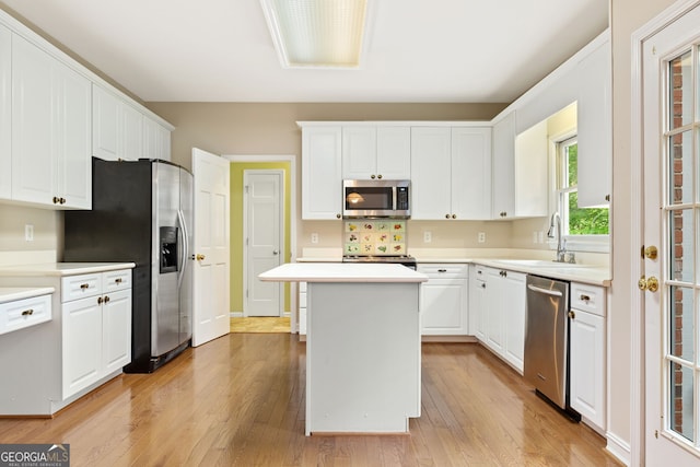 kitchen with appliances with stainless steel finishes, a sink, light wood-type flooring, and white cabinets