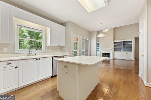 kitchen with stainless steel dishwasher, a sink, light wood-style flooring, white cabinetry, and a kitchen island