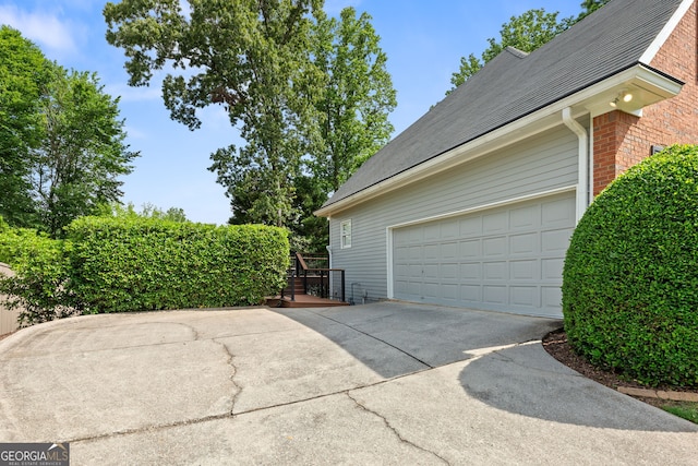 view of side of home featuring concrete driveway, brick siding, and a shingled roof