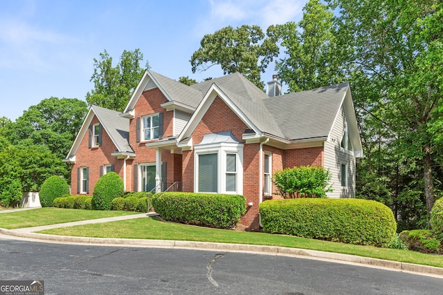traditional home featuring brick siding, a chimney, a front yard, and a shingled roof