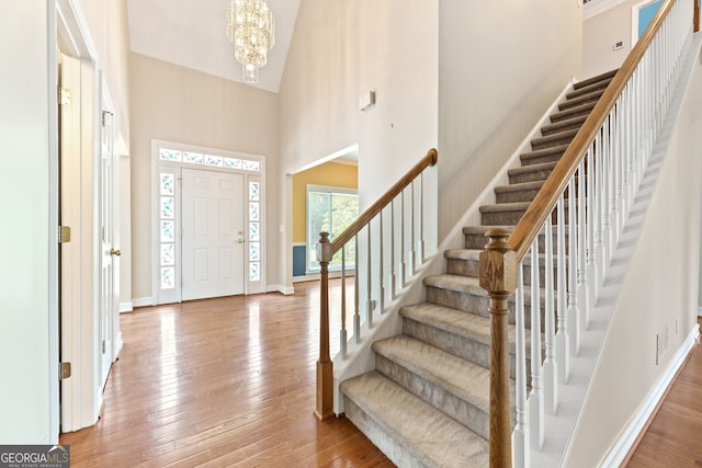 foyer featuring a high ceiling, stairs, a chandelier, hardwood / wood-style floors, and baseboards