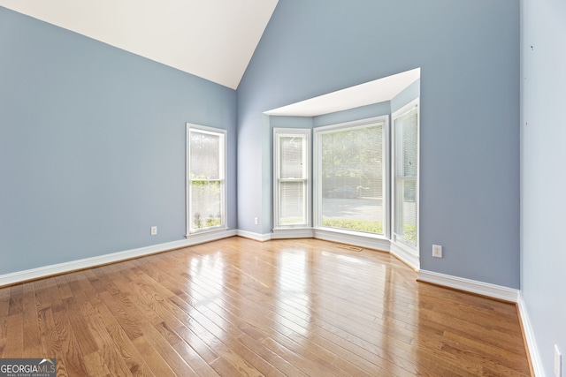 spare room featuring hardwood / wood-style floors, high vaulted ceiling, and baseboards