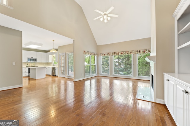 unfurnished living room with high vaulted ceiling, plenty of natural light, a fireplace, light wood-style flooring, and a ceiling fan