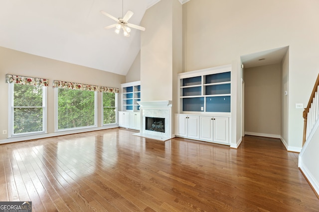 unfurnished living room featuring high vaulted ceiling, a fireplace, wood finished floors, ceiling fan, and stairway