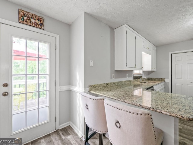 5293 Hopewell Ln, Gainesville, GA 30507 - kitchen with light wood finished floors, light stone counters, white cabinetry, a textured ceiling, and a peninsula