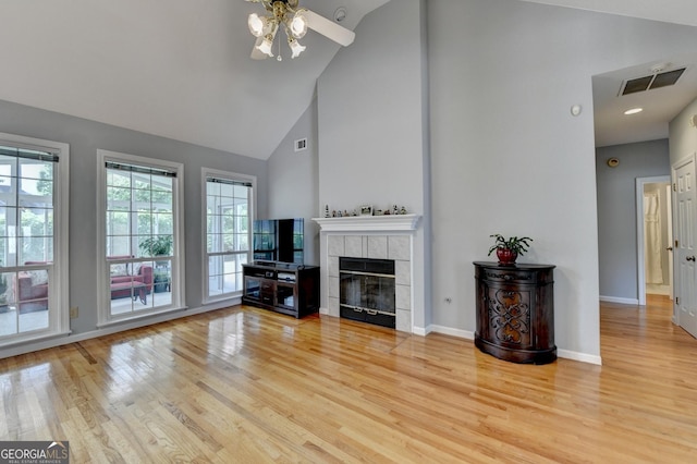 unfurnished living room featuring a ceiling fan, high vaulted ceiling, wood finished floors, baseboards, and a tile fireplace