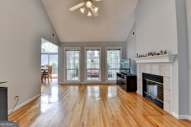 living room with high vaulted ceiling, ceiling fan, a tile fireplace, light wood-type flooring, and baseboards