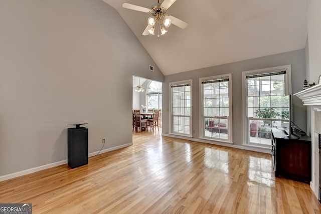 unfurnished living room featuring ceiling fan, high vaulted ceiling, light wood finished floors, baseboards, and a premium fireplace