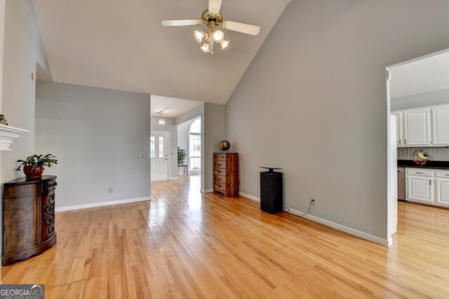 unfurnished living room with a ceiling fan, high vaulted ceiling, light wood-type flooring, and baseboards