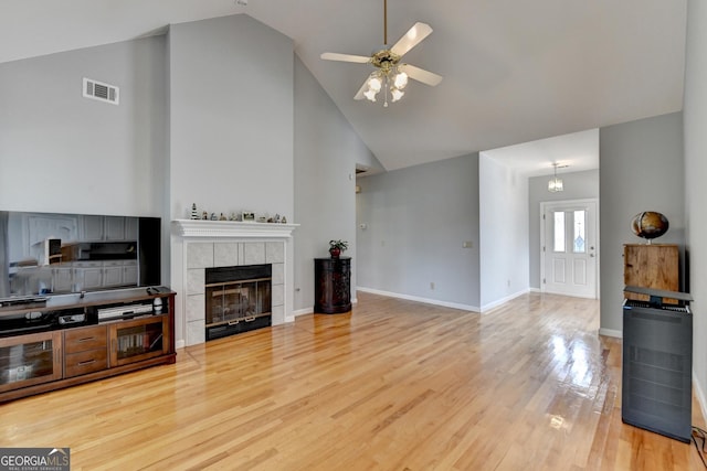 unfurnished living room featuring high vaulted ceiling, a ceiling fan, light wood-style flooring, a tiled fireplace, and baseboards