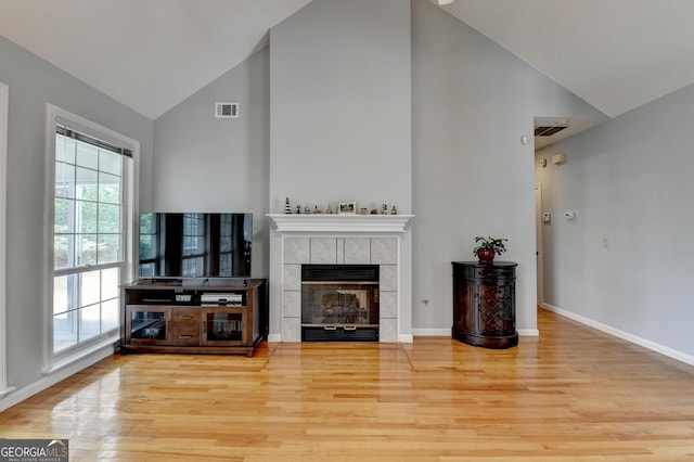 living area with high vaulted ceiling, wood finished floors, baseboards, and a tiled fireplace