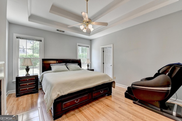 bedroom featuring a tray ceiling, crown molding, light wood-style floors, baseboards, and a ceiling fan