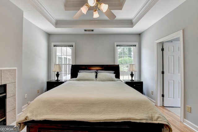 bedroom with crown molding, light wood finished floors, ceiling fan, baseboards, and a raised ceiling