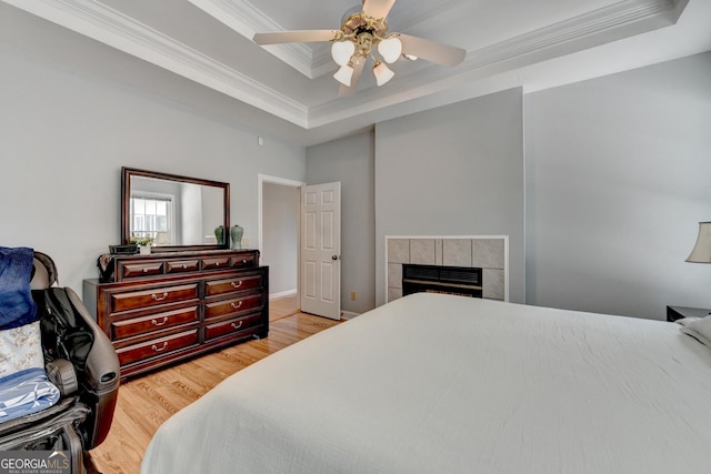 bedroom featuring a tray ceiling, ornamental molding, light wood-type flooring, a fireplace, and a ceiling fan