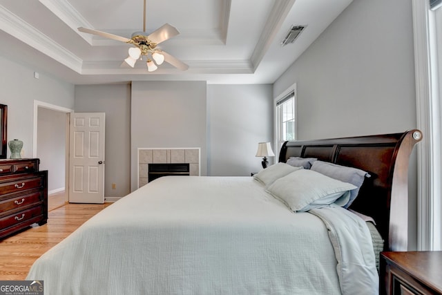 bedroom with a raised ceiling, crown molding, wood finished floors, a tile fireplace, and a ceiling fan