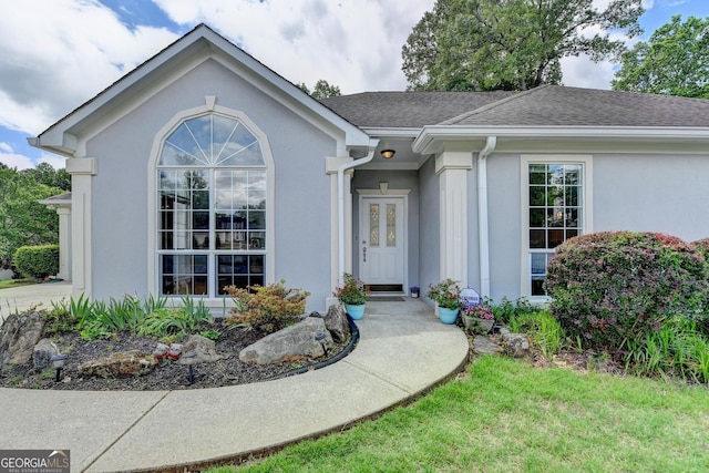 doorway to property with stucco siding and roof with shingles