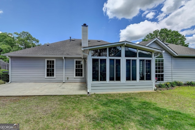 rear view of property featuring a patio, a chimney, a sunroom, a lawn, and roof with shingles