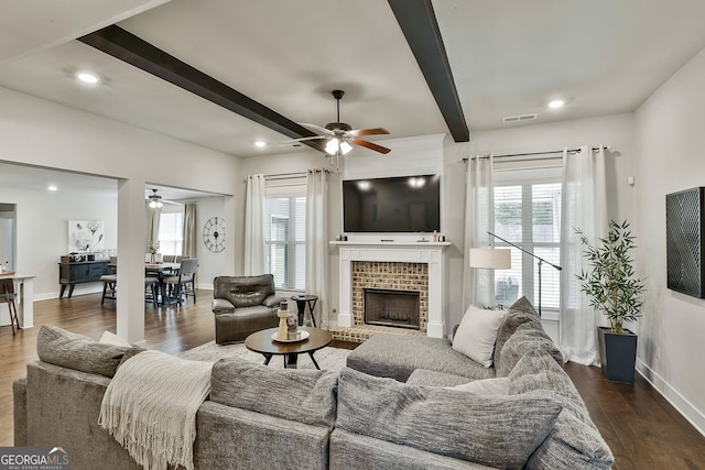living room featuring a ceiling fan, plenty of natural light, beamed ceiling, baseboards, and a brick fireplace
